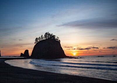 the sun is setting over the ocean with a rock formation in the foreground