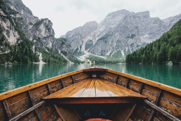Photo by Luca Bravo brown wooden boat moving towards the mountain